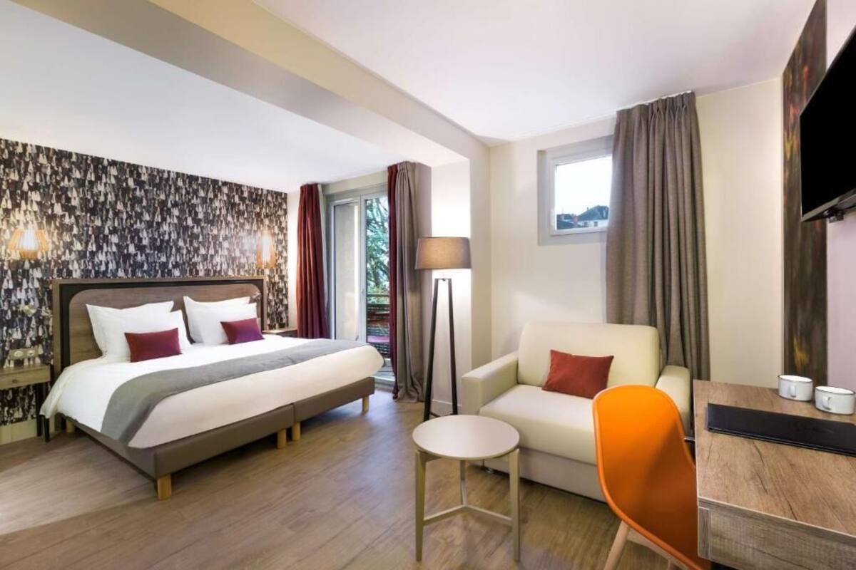 Une chambre d’hôtel avec un lit, un bureau, une chaise, une lampe et un téléviseur.