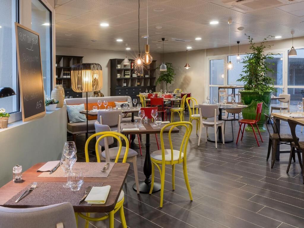 Un espace de restauration moderne avec des chaises jaunes, des tables en bois et des luminaires suspendus.