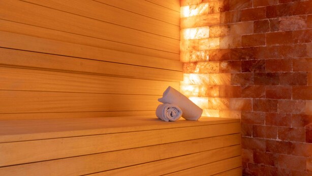 A wooden sauna bench with a rolled towel, a brick wall, and a wooden panel wall. - Best Western La Porte des Châteaux (Meung-sur-Loire)