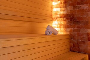 Un banc en bois dans un sauna, avec une serviette roulée, un mur en briques et un mur recouvert de panneaux en bois.