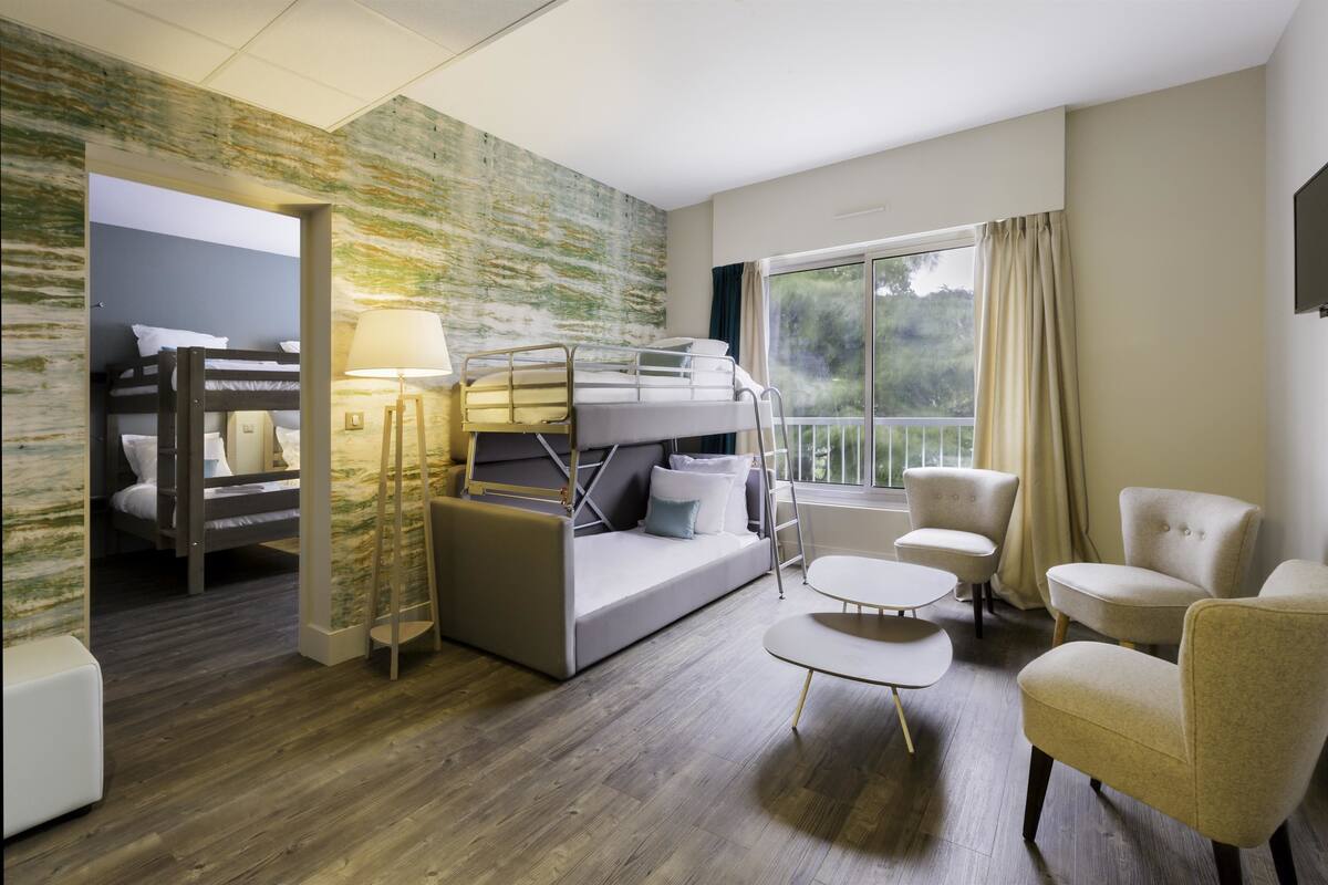 Une chambre d’hôtel moderne équipée d’un lit superposé, d’un canapé, d’une petite table et de deux fauteuils.
