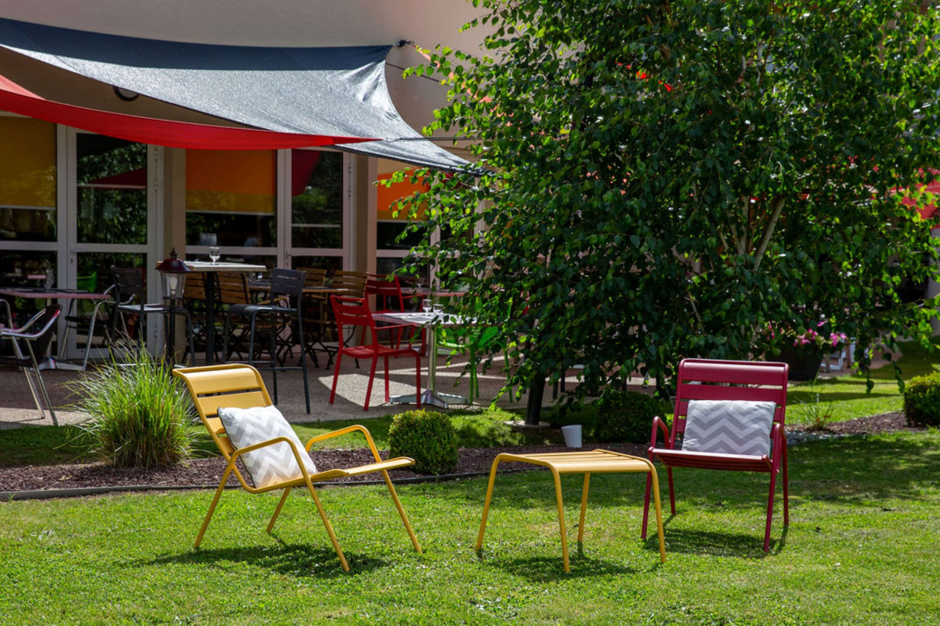 An outdoor seating area with yellow and red chairs, a covered patio, and a tree.