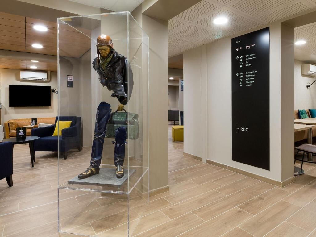 Un interior moderno con una vitrina que exhibe un maniquí vestido con ropa de invierno, una pizarra con información de la habitación y una zona de estar con sofá y mesa de centro.