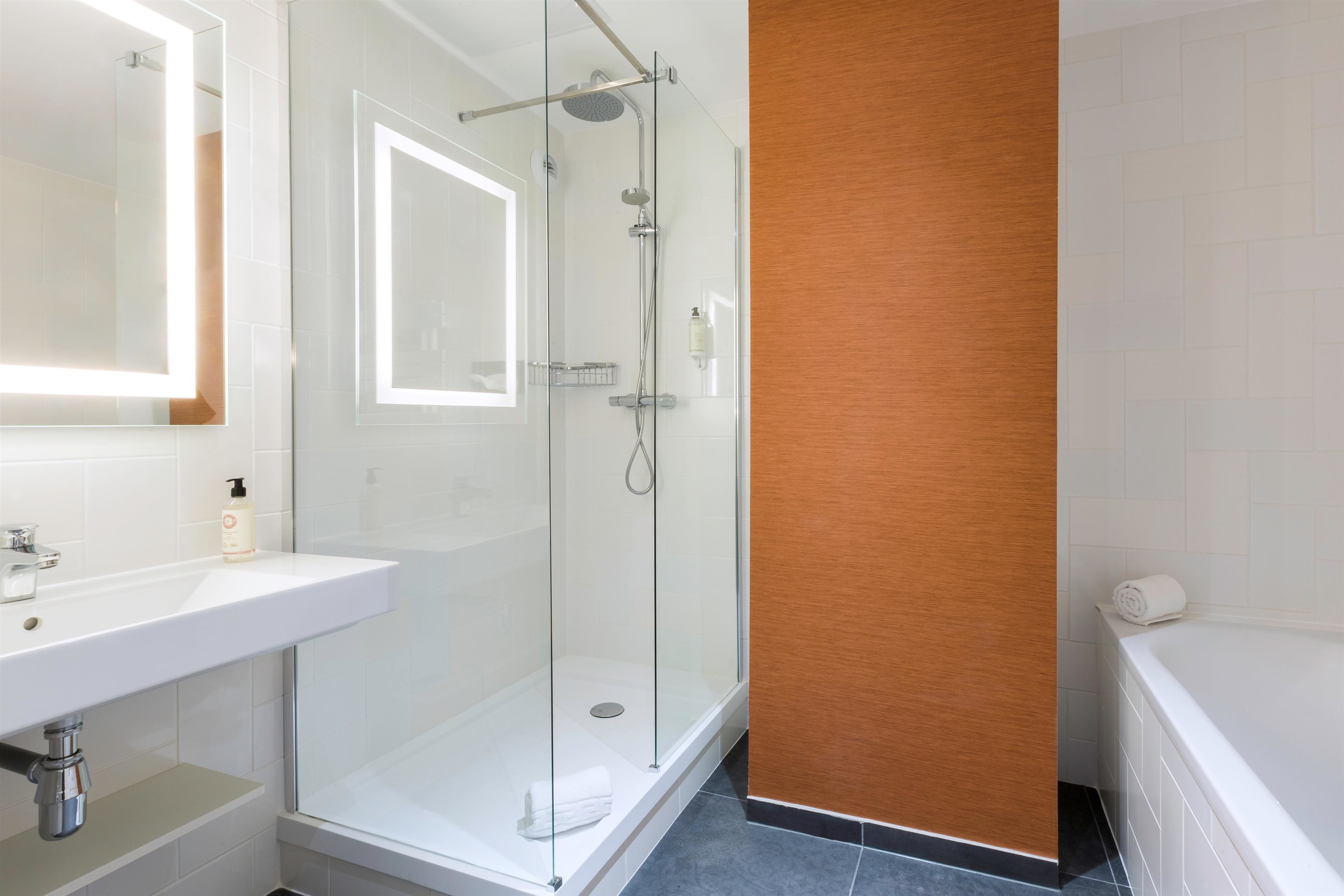 Un baño moderno con ducha envuelta en vidrio, lavamanos blanco y pared decorativa de madera.