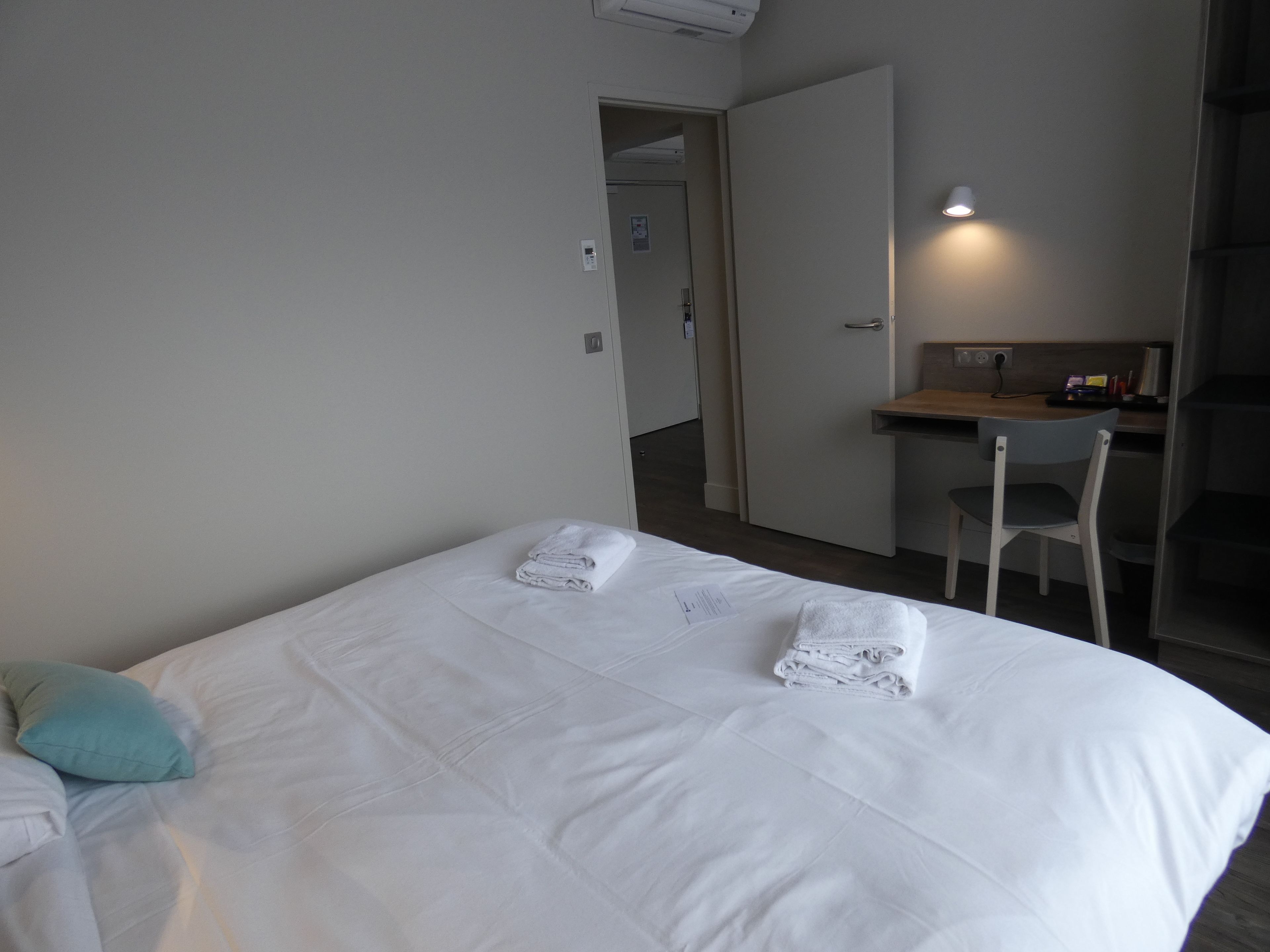 Quarto de hotel com cama, escrivaninha e cadeira.