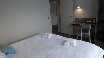 Quarto de hotel com cama, escrivaninha e cadeira.