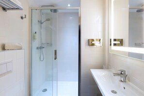 Een moderne badkamer met een glazen douchecabine, een witte wastafel en een grote spiegel.