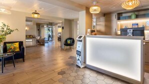 A hotel reception area with a modern design, featuring a reception desk, a seating area with a sofa and a small table, and a decorative plant. - Best Western La Porte des Châteaux (Meung-sur-Loire)