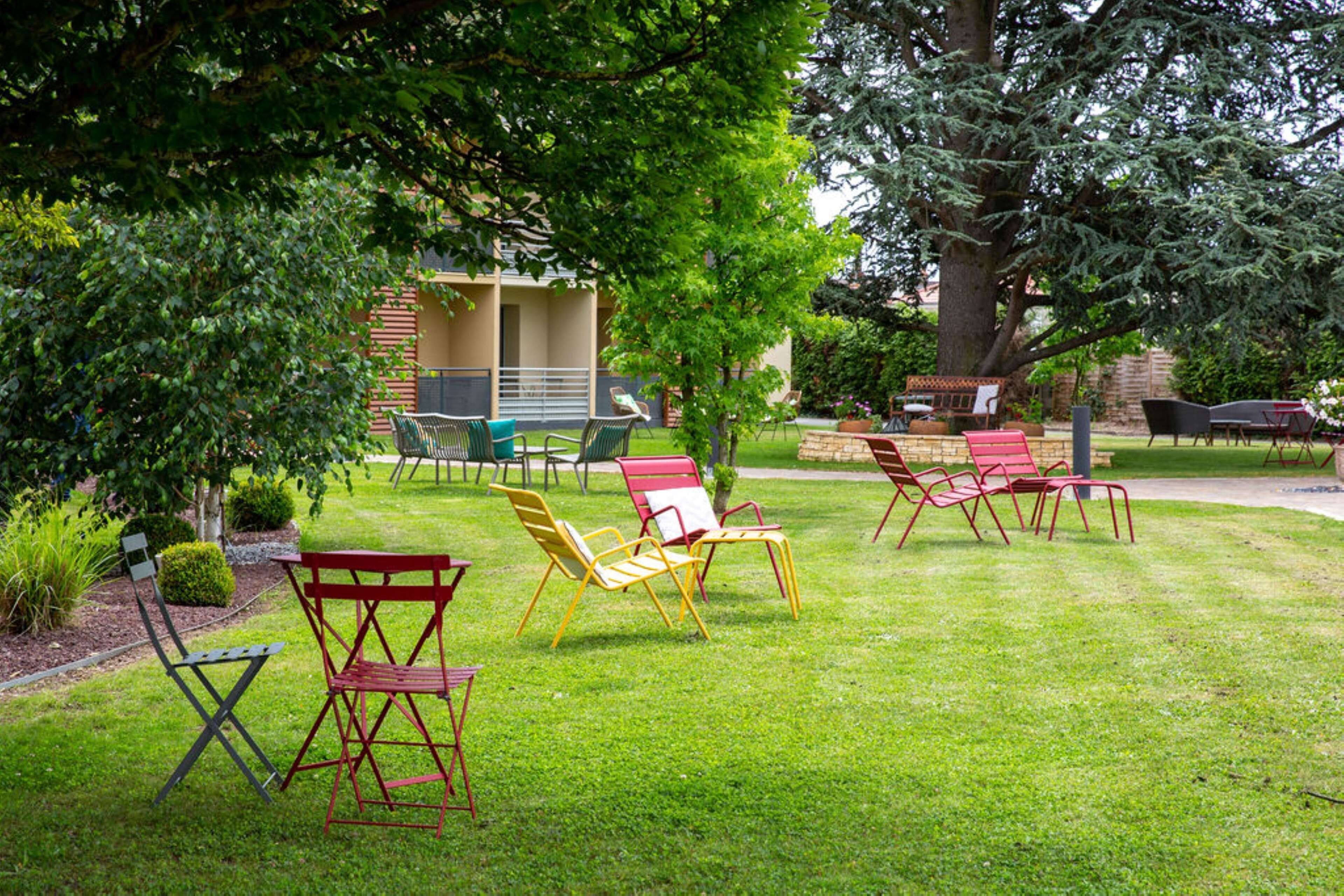 An outdoor seating area with multiple chairs and tables, surrounded by greenery and trees.