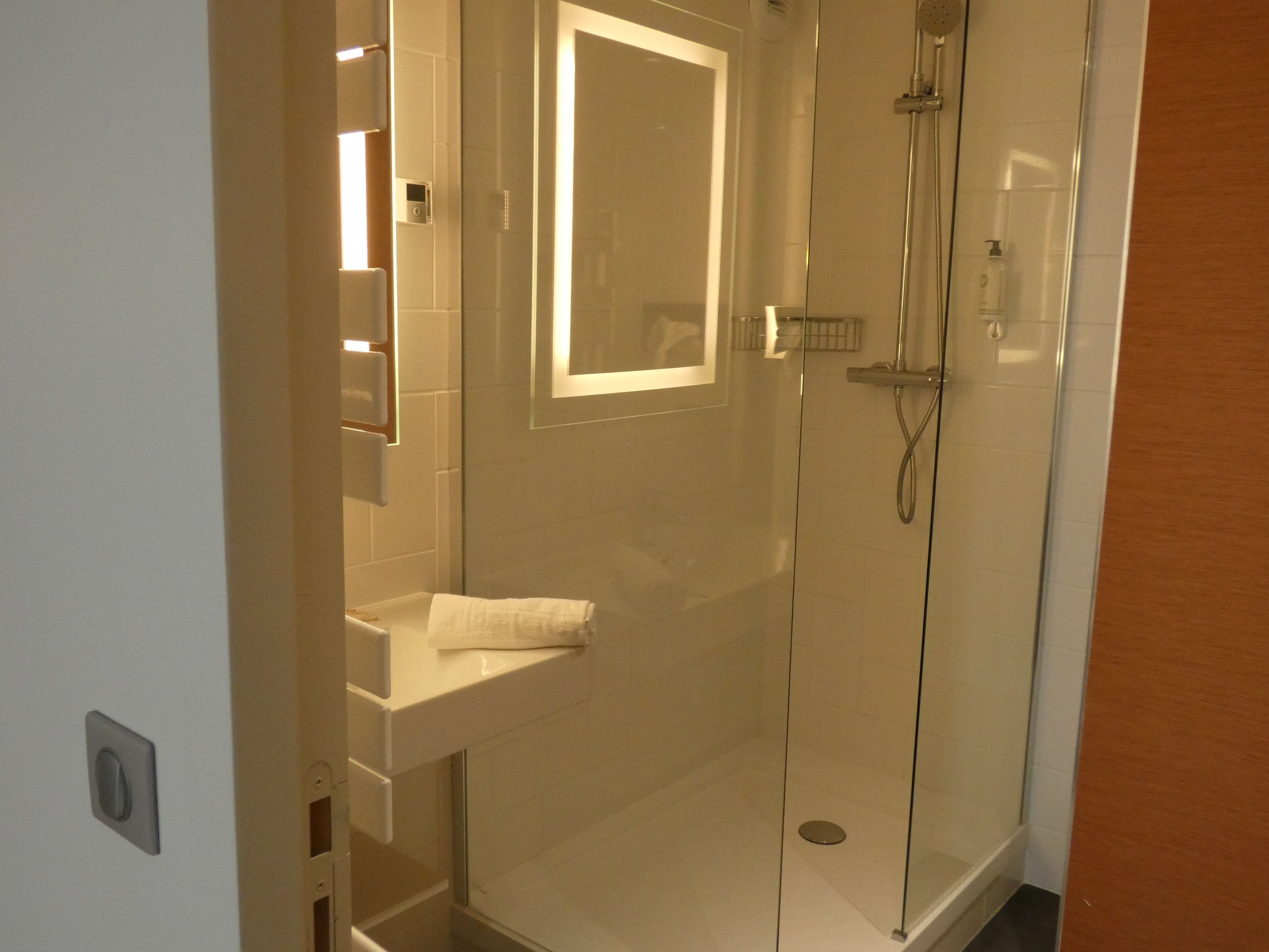 A glass-enclosed shower with a handheld showerhead and a wall-mounted faucet.