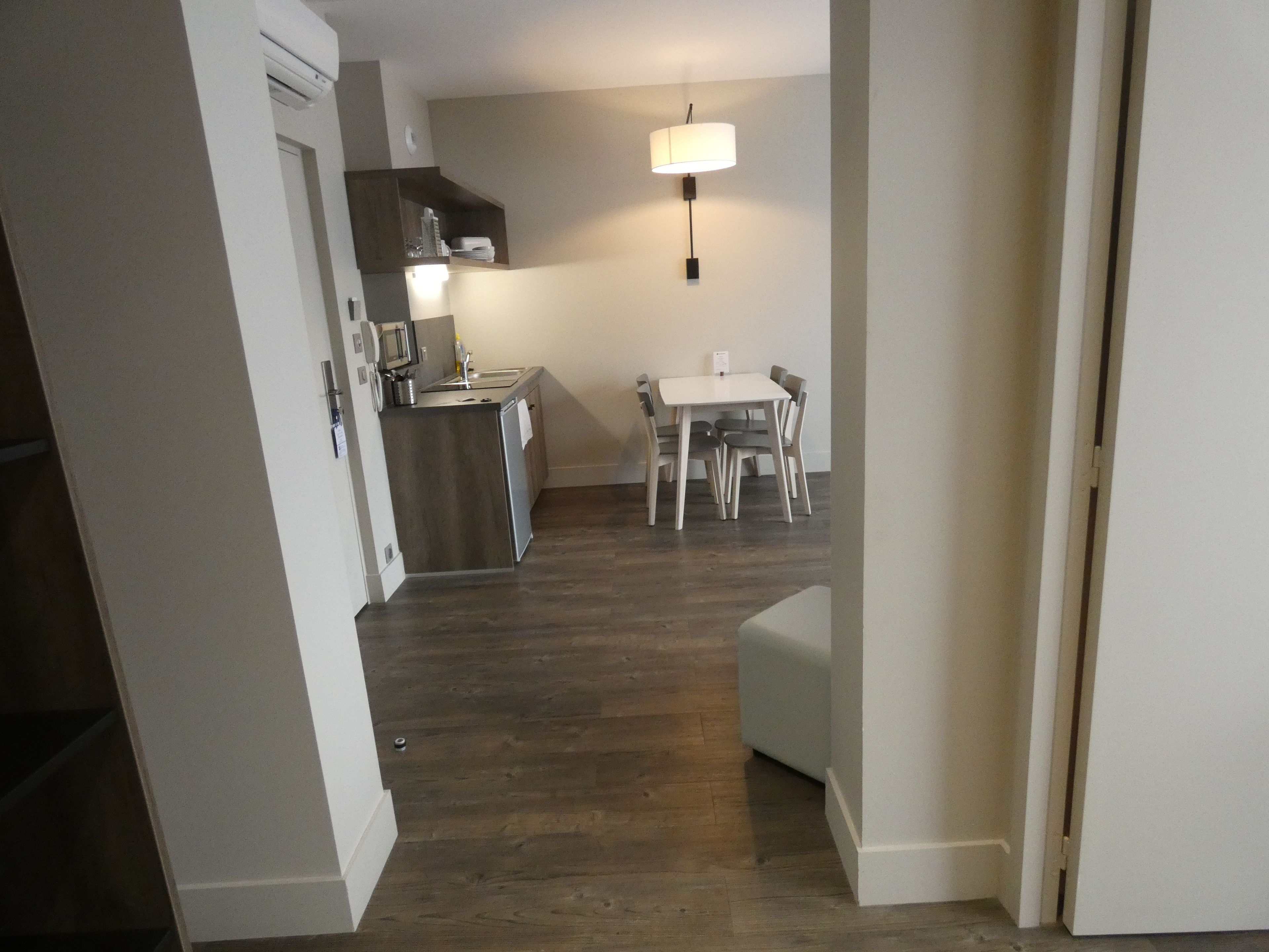A modern kitchen with a microwave, stove, and sink, a dining area with a table and chairs, and a hallway leading to another room.