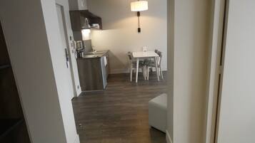 A modern kitchen with a microwave, stove, and sink, a dining area with a table and chairs, and a hallway leading to another room.