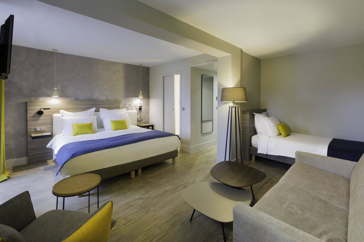 Une chambre d’hôtel moderne avec un grand lit, un canapé, une petite table et une lampe.
