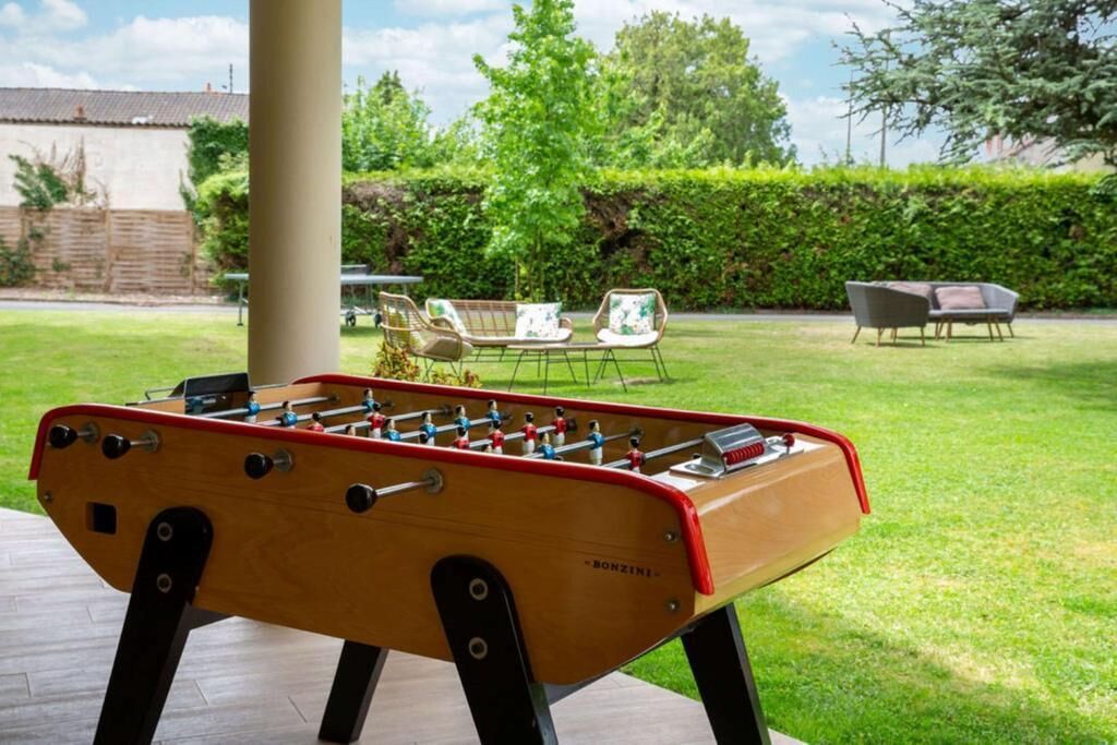 Una mesa de fútbol de mesa en un área exterior con césped, con sillas y una mesa al fondo.