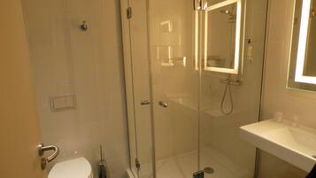 Een moderne badkamer met een douche met glazen wand, een wit wastafelmeubel en een toilet.