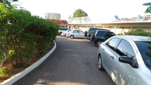 Ein Parkplatz mit mehreren Autos, die entlang eines gewundenen Weges stehen, umgeben von Grünflächen und einem Gebäude mit rotem Dach im Hintergrund.