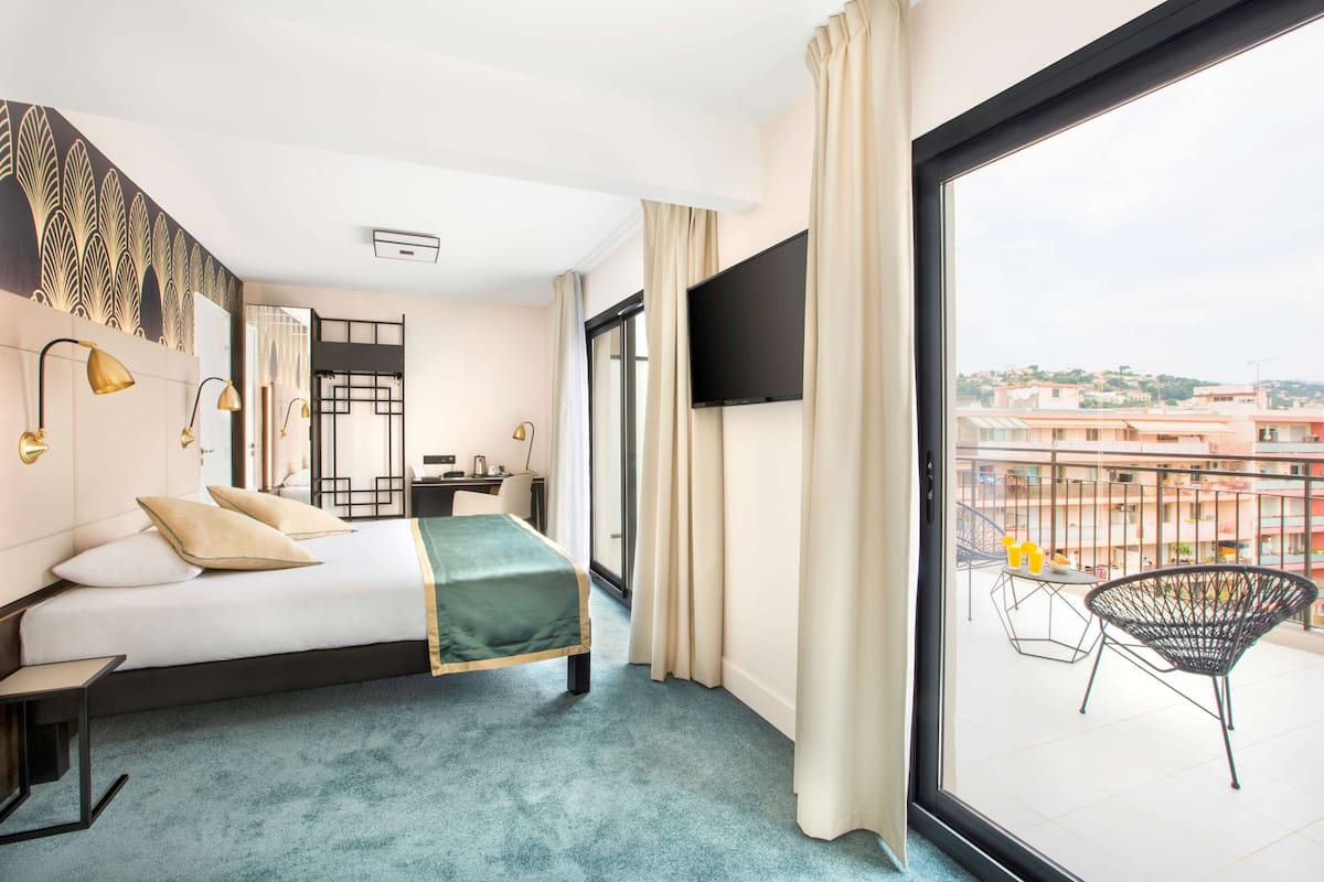 Habitación de hotel con cama, escritorio, silla, televisor y balcón con una silla y una mesa.