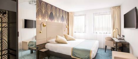 A hotel room with a large bed, a desk, a chair, a TV, and a mirror.