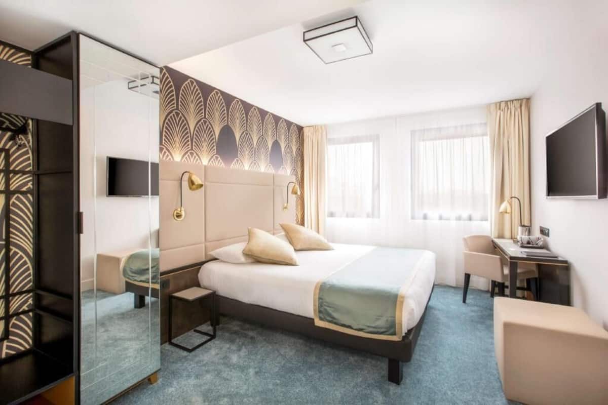 Una habitación de hotel con una cama grande, un escritorio, una silla, un televisor y un espejo.