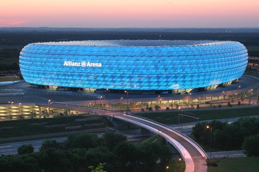 A stadium with a distinctive blue, geodesic dome roof and the text "Allianz Arena" on it.