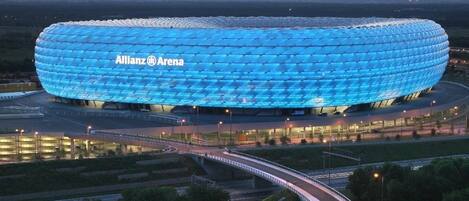 A stadium with a distinctive blue, geodesic dome roof and the text "Allianz Arena" on it.