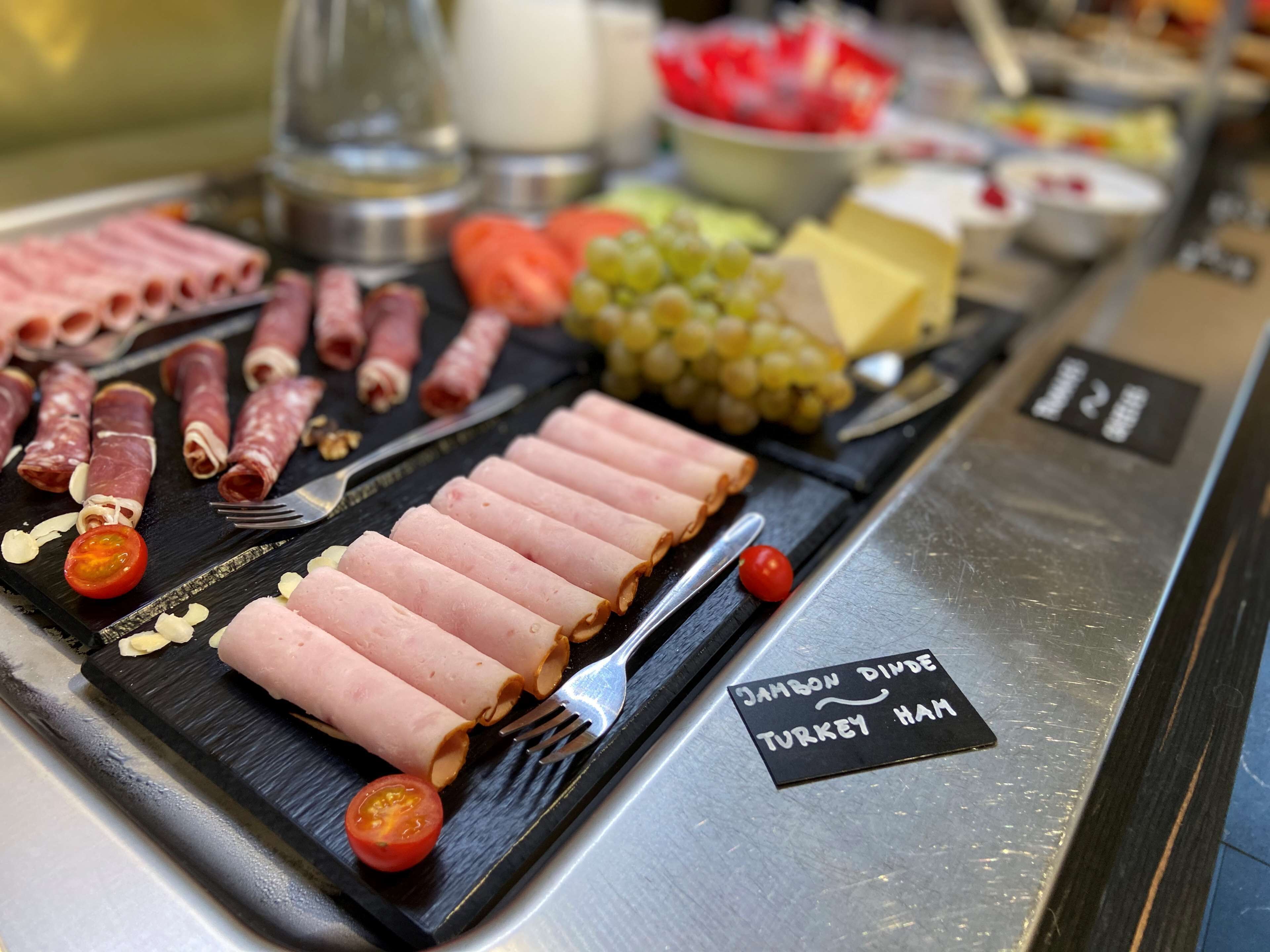 Eine Platte mit verschiedenen Fleisch- und Käsesorten, darunter Putenbrust, auf einer schwarzen Schieferplatte.