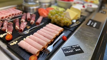 Eine Platte mit verschiedenen Fleisch- und Käsesorten, darunter Putenbrust, auf einer schwarzen Schieferplatte.