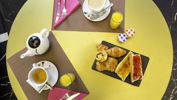 A breakfast setting with a teapot, cup, croissants, and juice on a table.