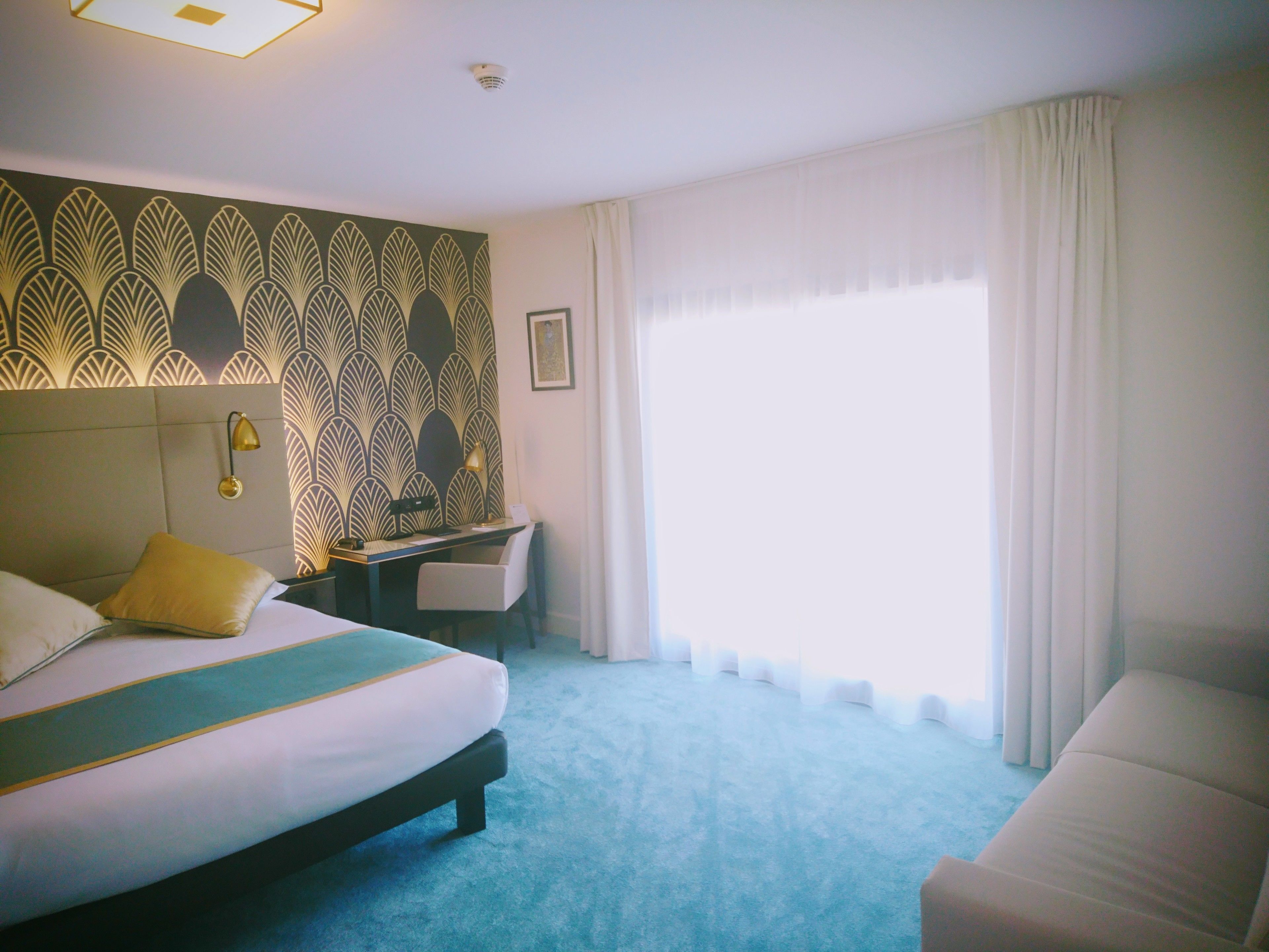 A hotel room with a bed, a desk, a chair, and a large window with curtains.
