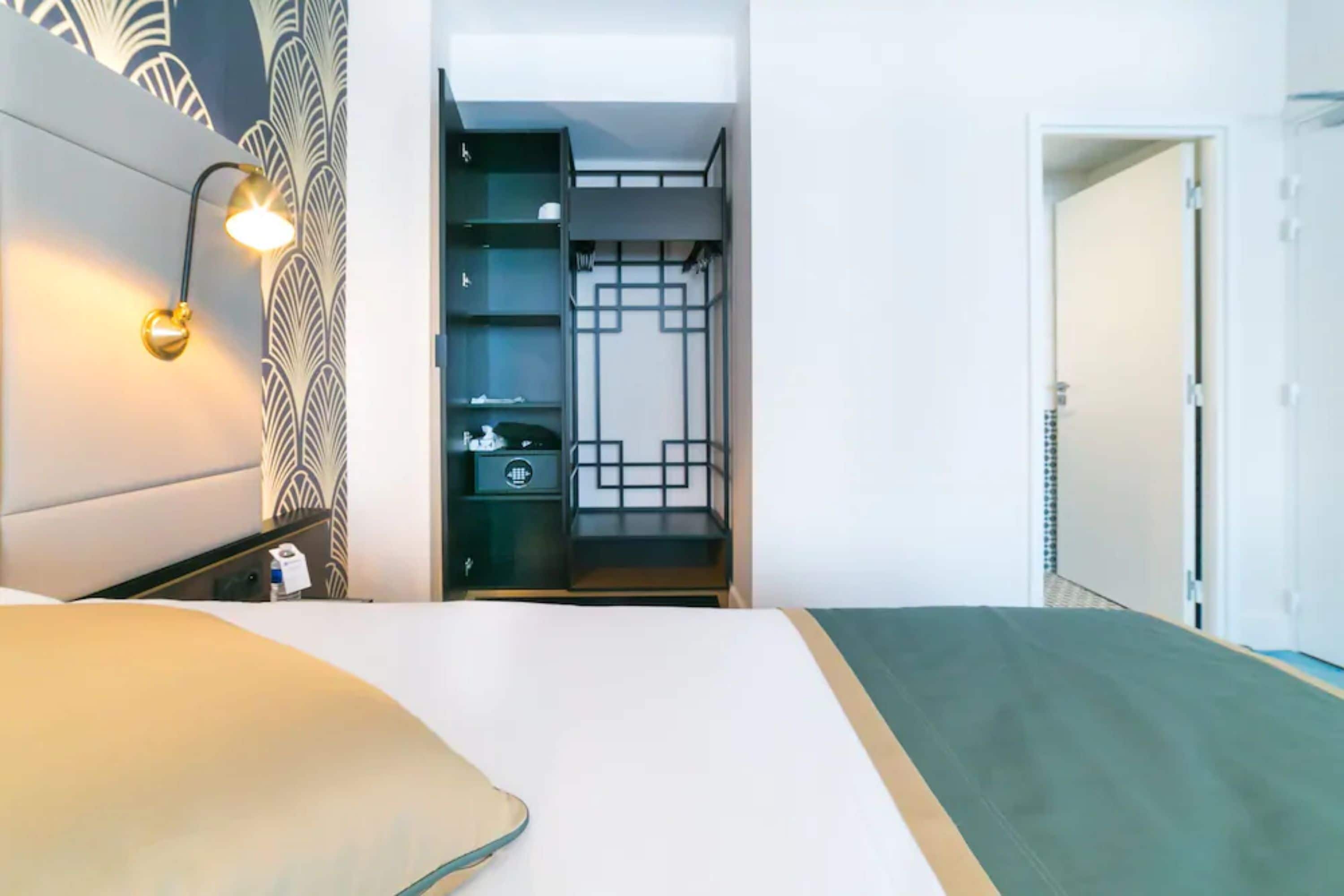 Una habitación de hotel con cama, mesita de noche, lámpara y armario con espejo.