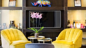 Un hall con dos sillones amarillos, un sofá gris, un televisor plano grande, una planta en maceta y una escultura decorativa de un rinoceronte.