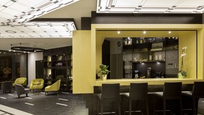 Un área de bar moderna con una pared de acento amarilla, taburetes negros y una vitrina de vidrio con botellas.