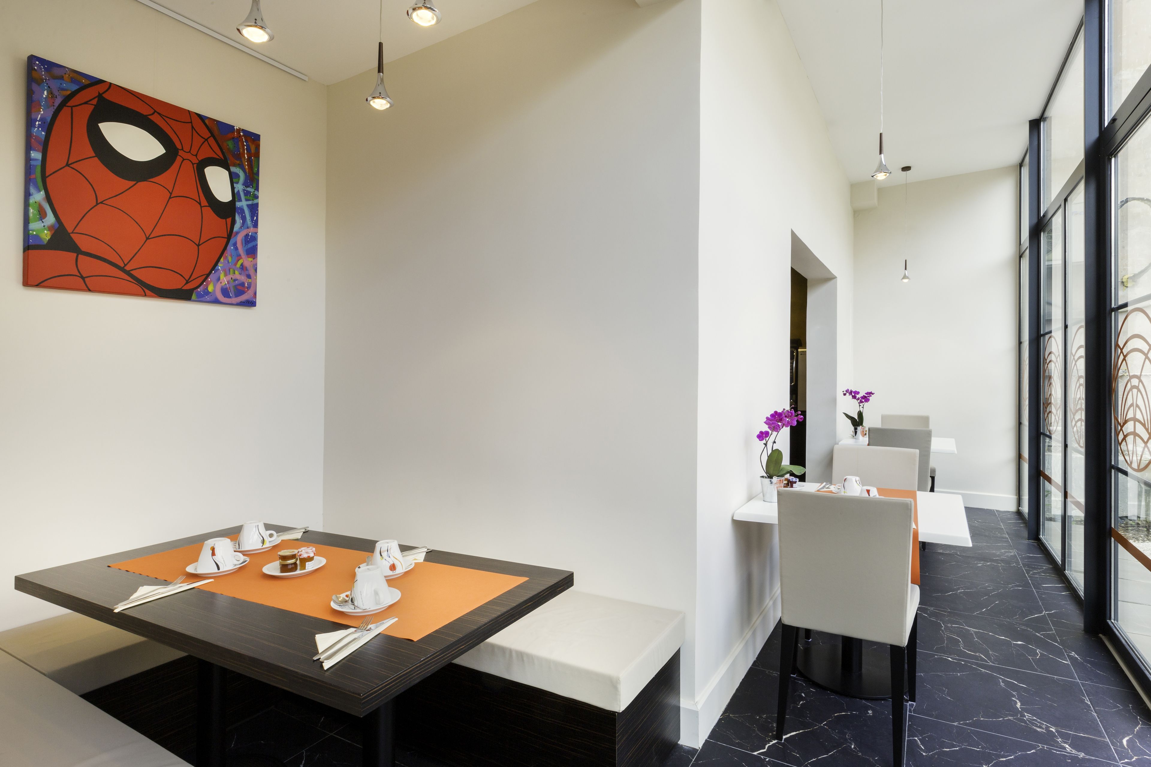 Un comedor moderno con una mesa preparada para dos personas, una obra de arte de Spiderman en la pared y vistas amplias a través de grandes ventanales.