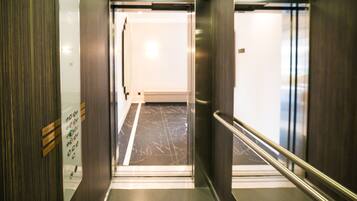 Elevatorinteriør med marmorgulv, metalgelændere og et kontrolpanel med knapper.