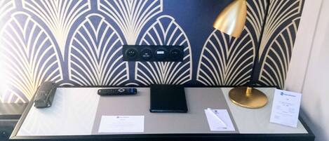 A desk with a lamp, remote controls, and papers.