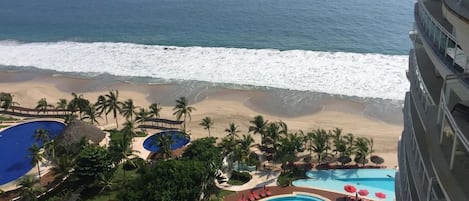 A resort with a large pool area, palm trees, and a view of the ocean.
