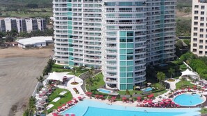 Un hotel de gran altura con varias plantas, una piscina y una zona ajardinada con palmeras.