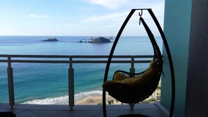 Un balcón con una silla colgante con vista a la playa y al mar.