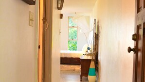 A hallway leading to a bedroom with a bed, a nightstand, a vase, and a window with a view of greenery. - Crystal Beach Studio (Montego Bay)