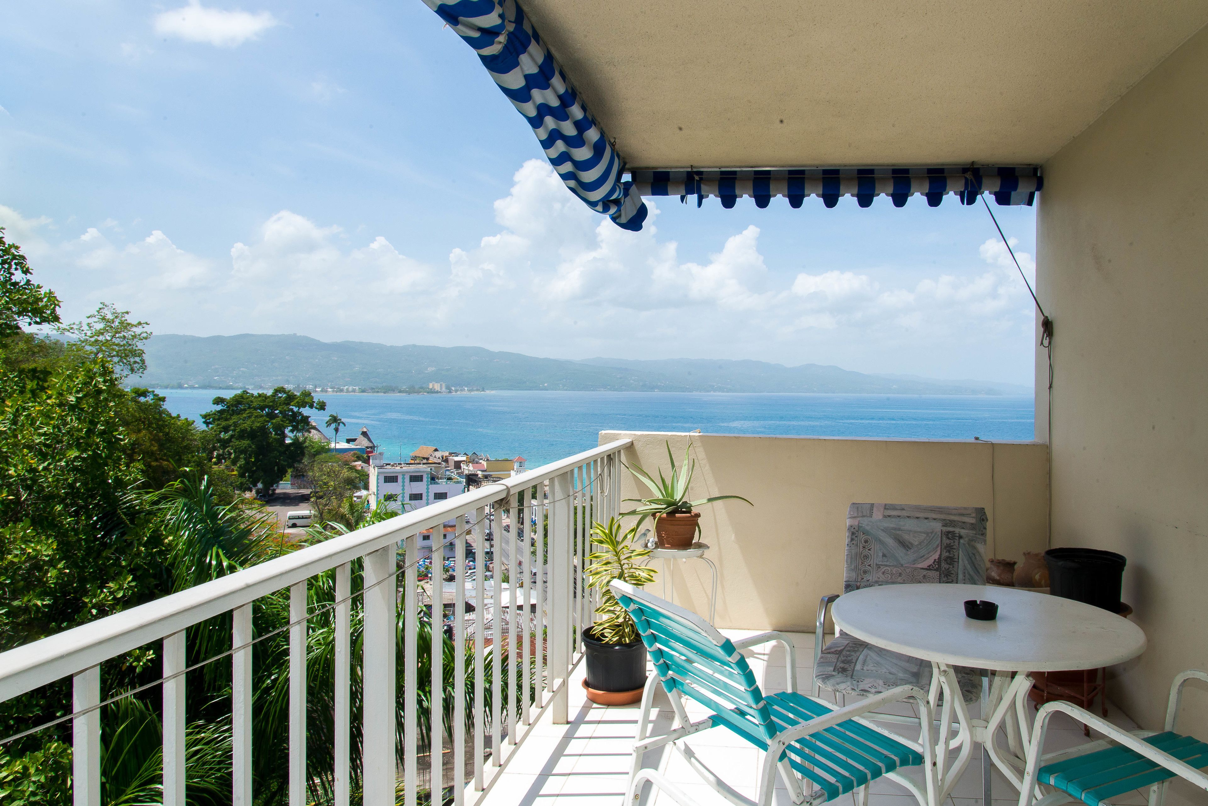 A balcony with a white railing, a table with chairs, and potted plants.