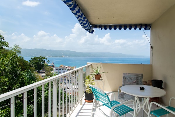 A balcony with a white railing, a table with chairs, and potted plants.