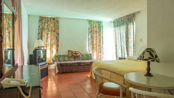 A hotel room with a bed, a sofa, a small table, a telephone, and a television.