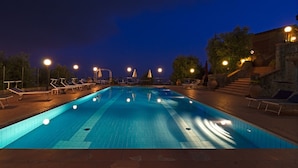 A swimming pool with lounge chairs and lights at night. - I Sette Borghi (Massa e Cozzile)