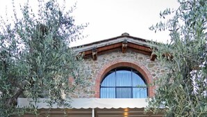A stone building with a large arched window and a covered patio area with tables and chairs. - I Sette Borghi (Massa e Cozzile)