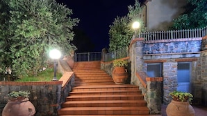 A set of stone steps leading to a building with a stone facade, flanked by large terracotta pots and illuminated by street lamps. - I Sette Borghi (Massa e Cozzile)