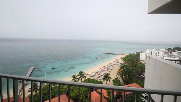 A beach view from a balcony with a clear sky, a sandy beach, and a pier extending into the water. - Hipstrip Beach Studio (Montego Bay)