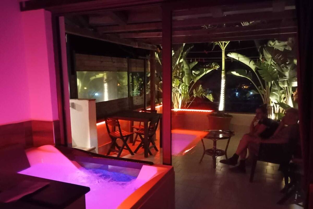 A room with a glass partition, a massage table, and a seating area with chairs and a table.