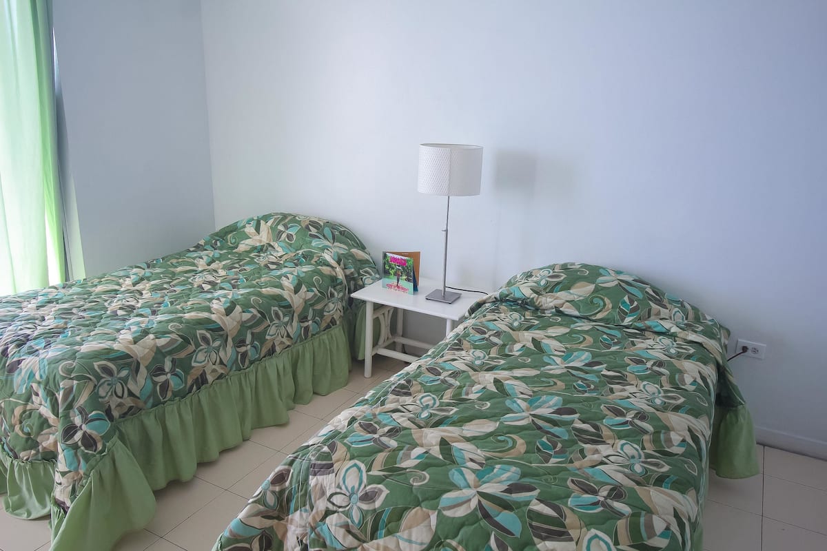A bedroom with two beds, a bedside table with a lamp, and a small table with a picture frame and a book.