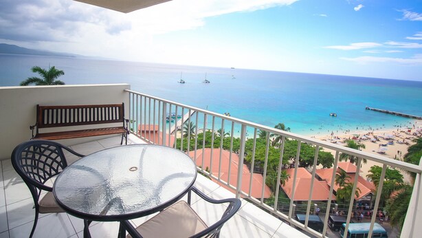 A balcony with a table and chairs, overlooking a beach with boats and a pier. - Irie Beach Studio (Montego Bay)