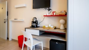Cocina compacta con cafetera, un televisor sobre la encimera y un pequeño comedor con una silla y un taburete rojo.